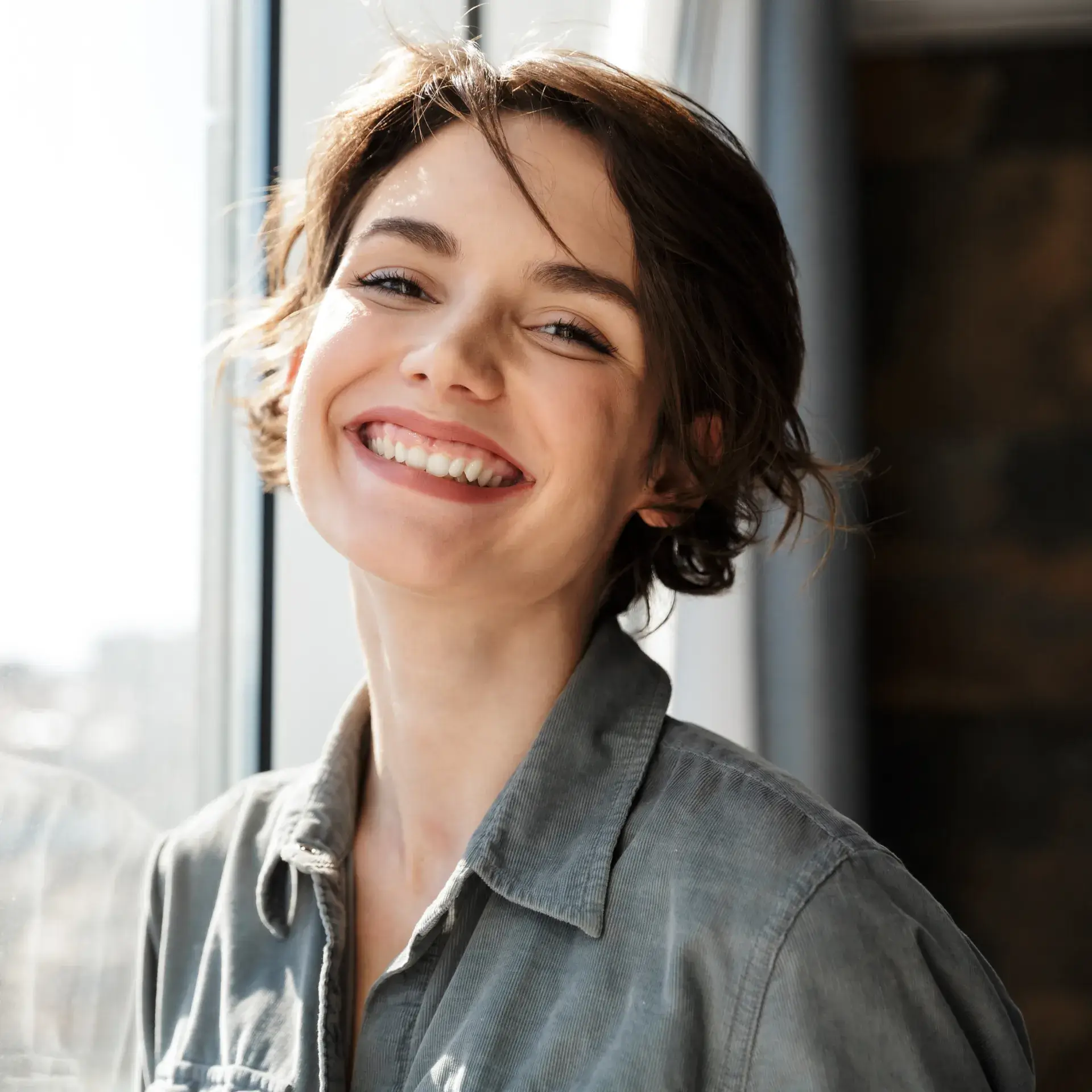 A woman smiling and looking out of a window.