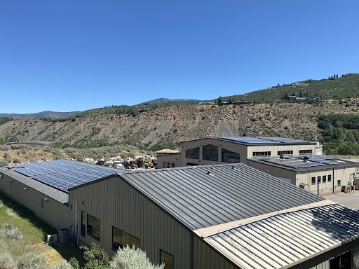 Rooftop solar panels on Pitkin County Public Works shop buildings, with a dry hillside behind