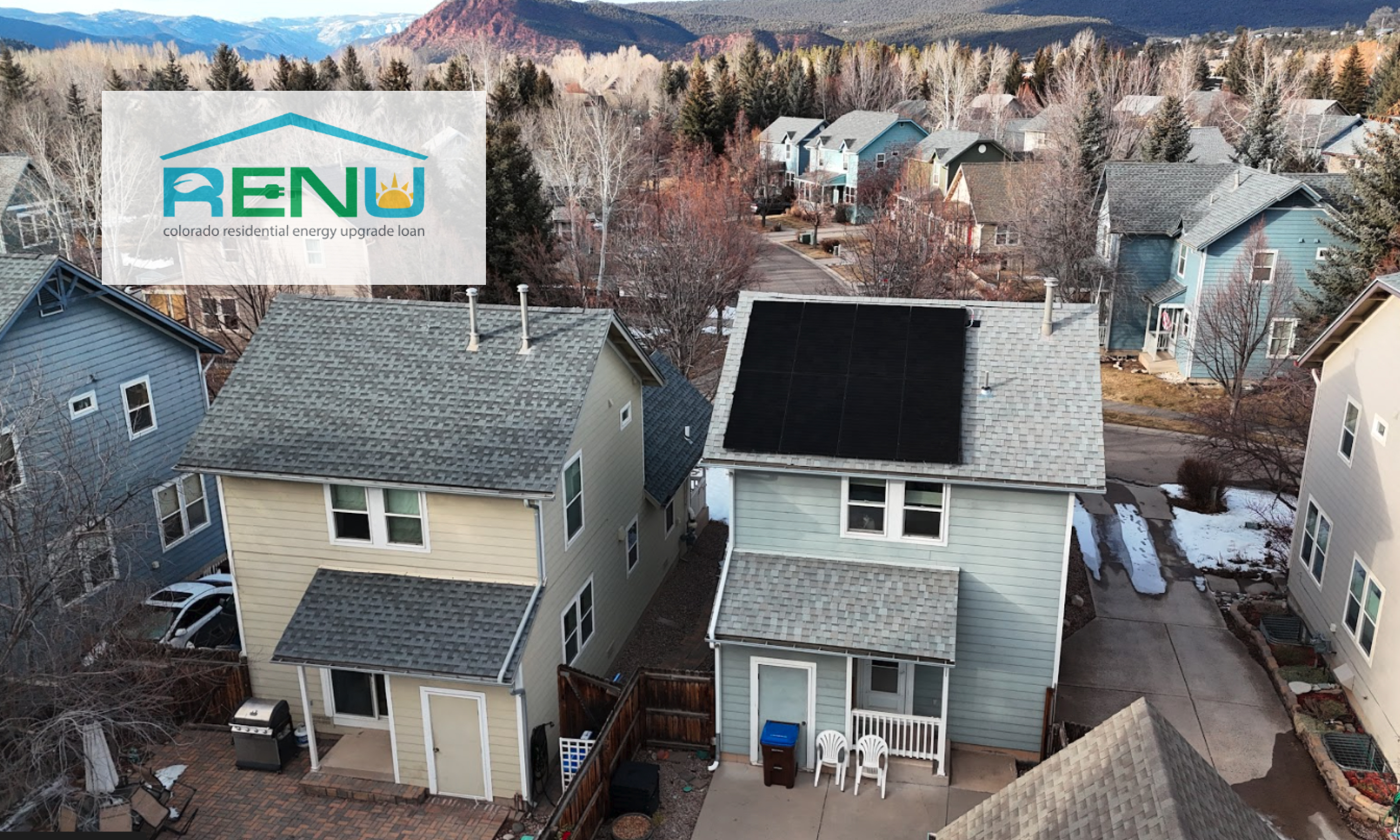 Aerial view of houses in a mountain town, one with solar panels on its roof, with a RENU loan logo overlay