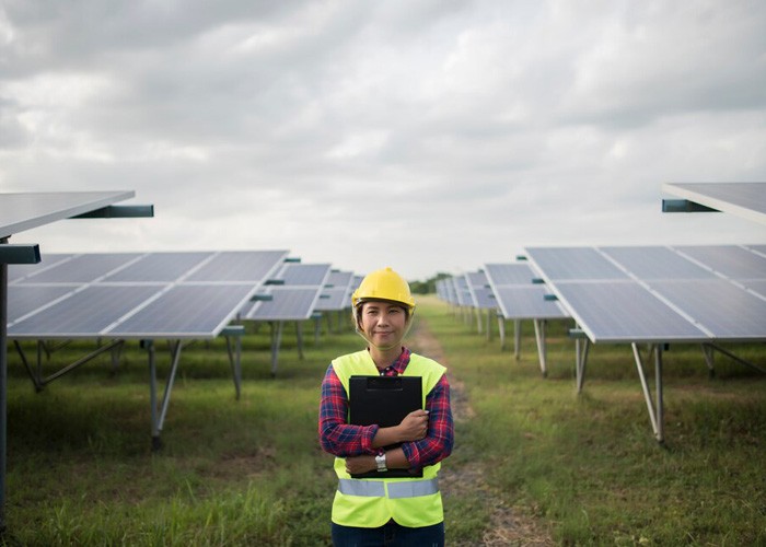 Worker in a hard hat and safety vest holding a clipboard in a field of solar panels