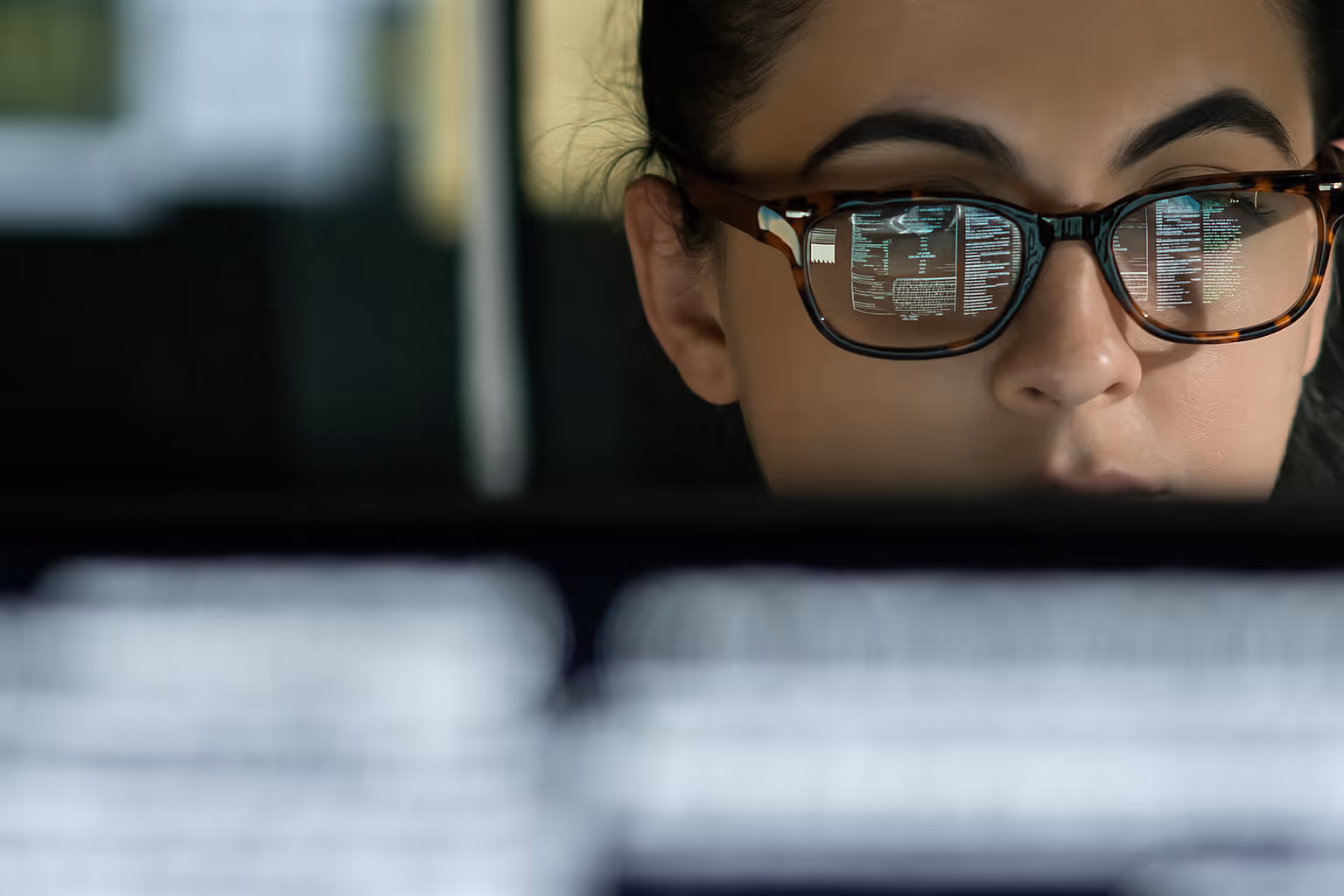 Close-up of a woman wearing glasses with computer code reflected in the lenses.