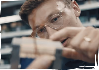 Junger Mann mit Brille fokussiert auf ein Holzobjekt, das er mit den Fingern hält.