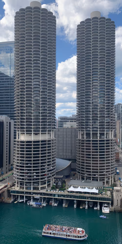 Two tall cylindrical skyscrapers with curved balconies overlooking a body of water with a tour boat.