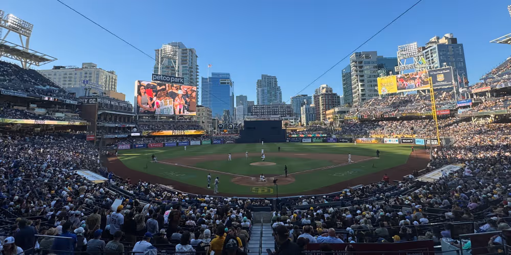 Panoramic view of a baseball game in progress at Petco Park stadium filled with spectators under a clear blue sky.