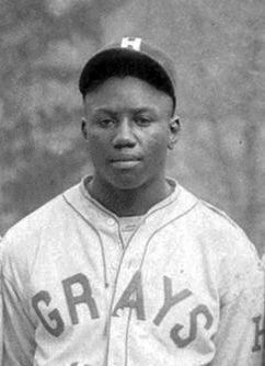 Black-and-white photo of a young African American baseball player wearing a Grays uniform and cap.