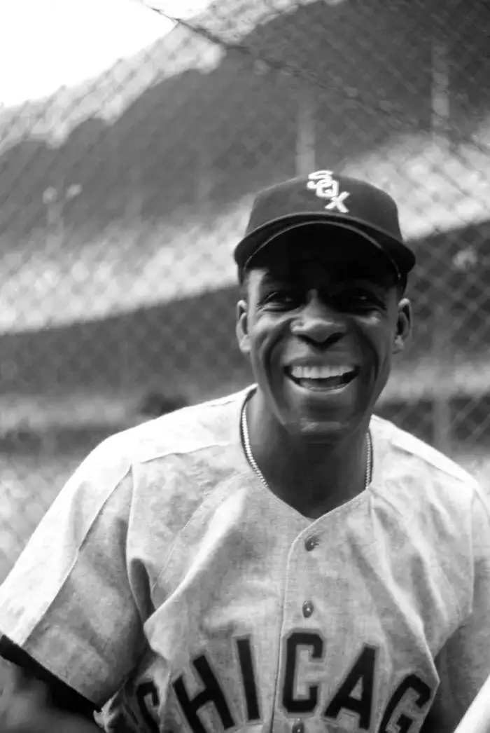 Smiling baseball player wearing a Chicago White Sox uniform and cap, standing in front of a chain-link fence.