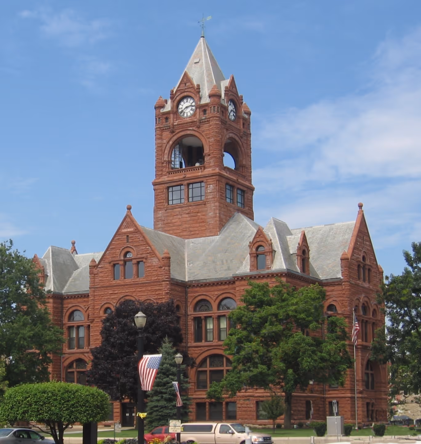 Historic red brick courthouse building with a tall clock tower and a pointed roof under a blue sky.