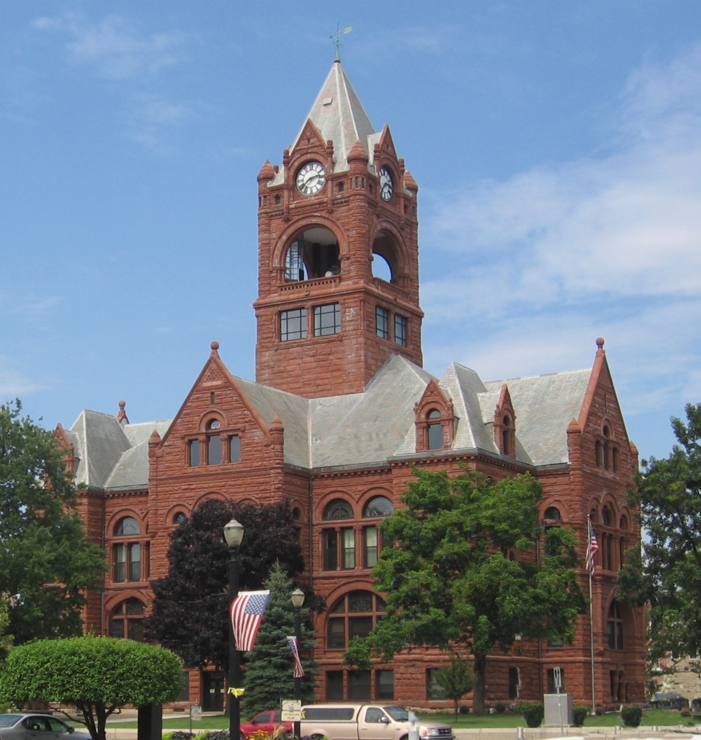 Historic red brick courthouse building with a tall clock tower and a pointed roof under a blue sky.