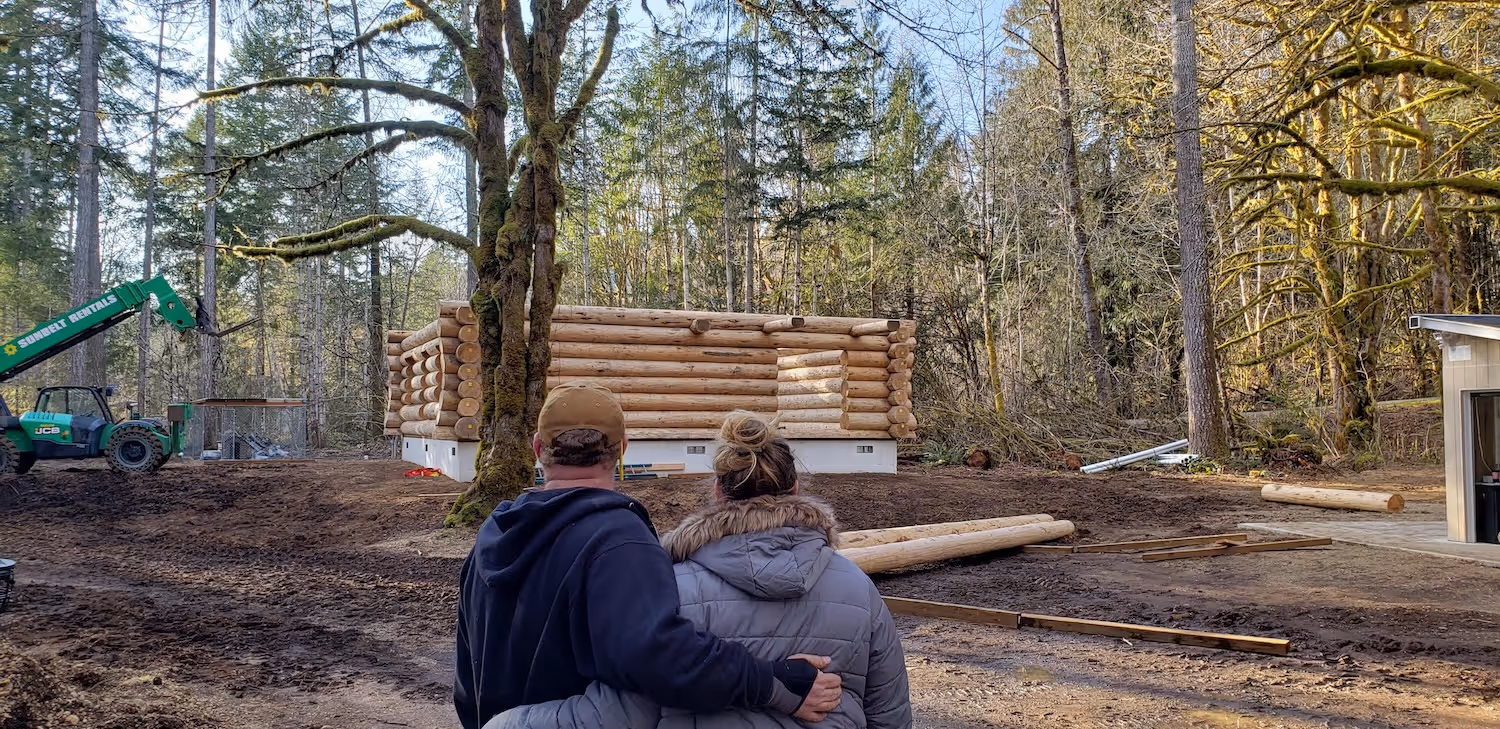 A man and a woman standing in front of a pile of logs.
