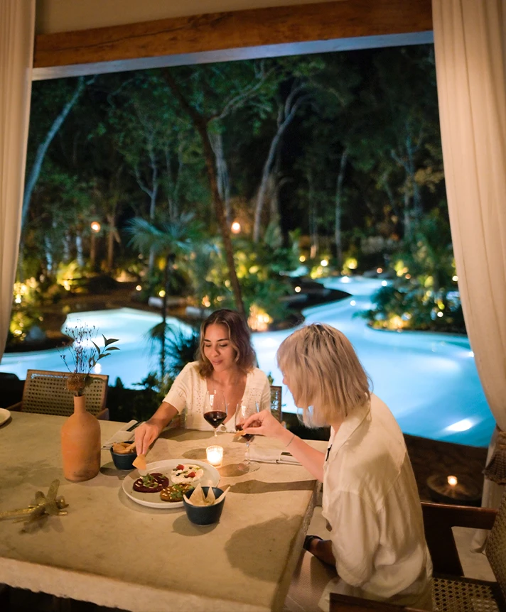 dos mujeres sentadas a una mesa con comida y una piscina al fondo