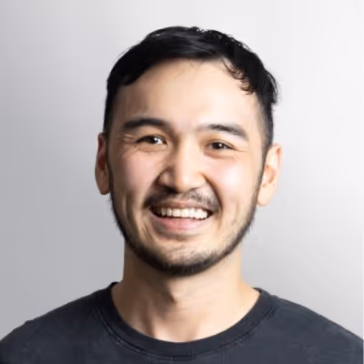 Smiling man with short dark hair and a beard wearing a black shirt against a light gray background.