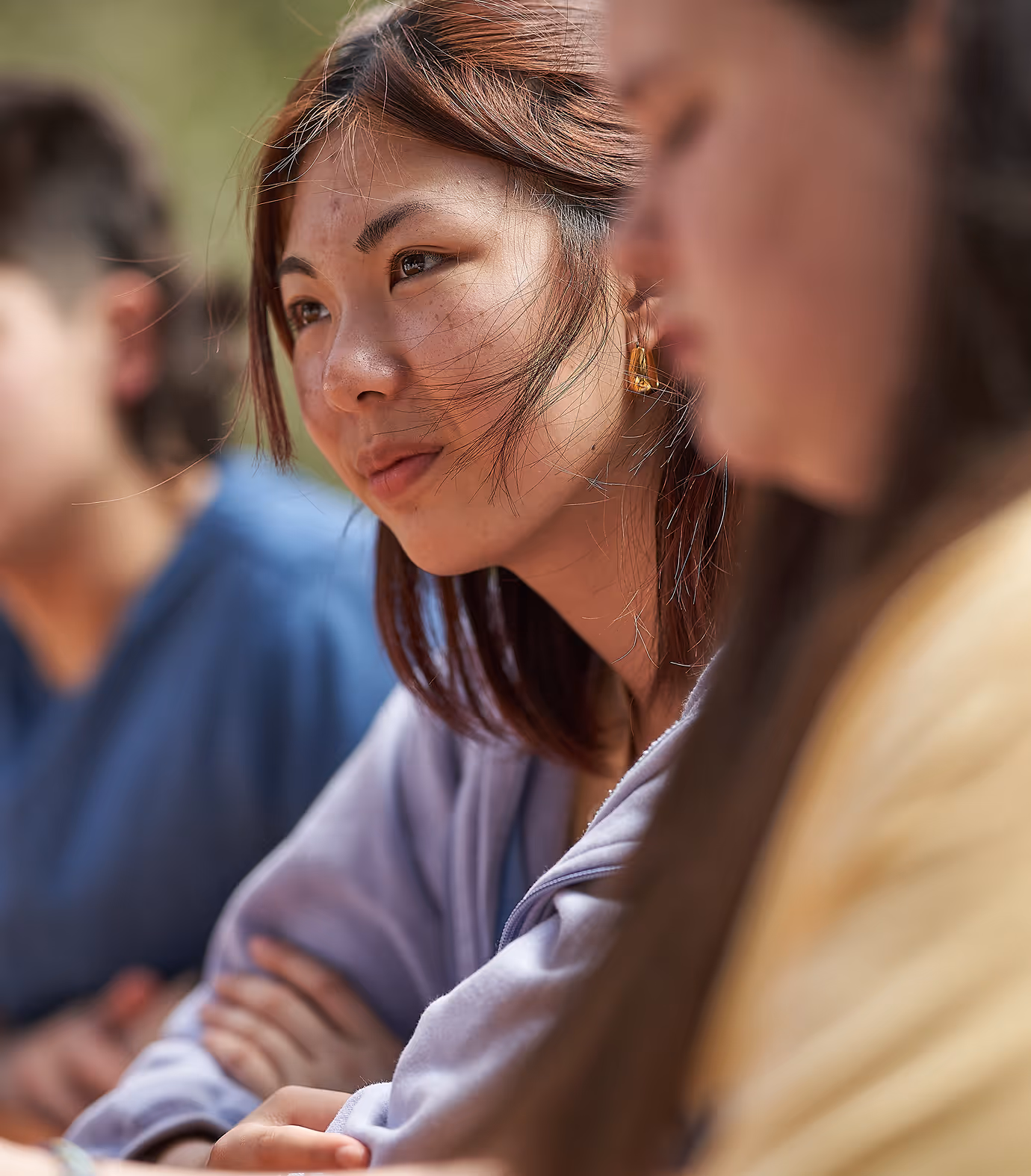 Group of young people sitting outside around a table, focus on one young girl