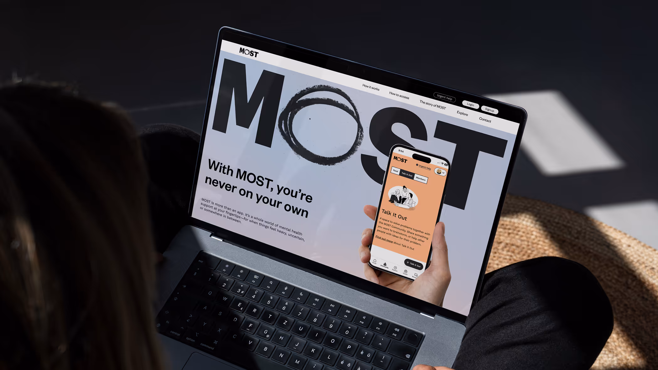 Person sitting on ground with laptop on their lap, with the MOST website is on the screen