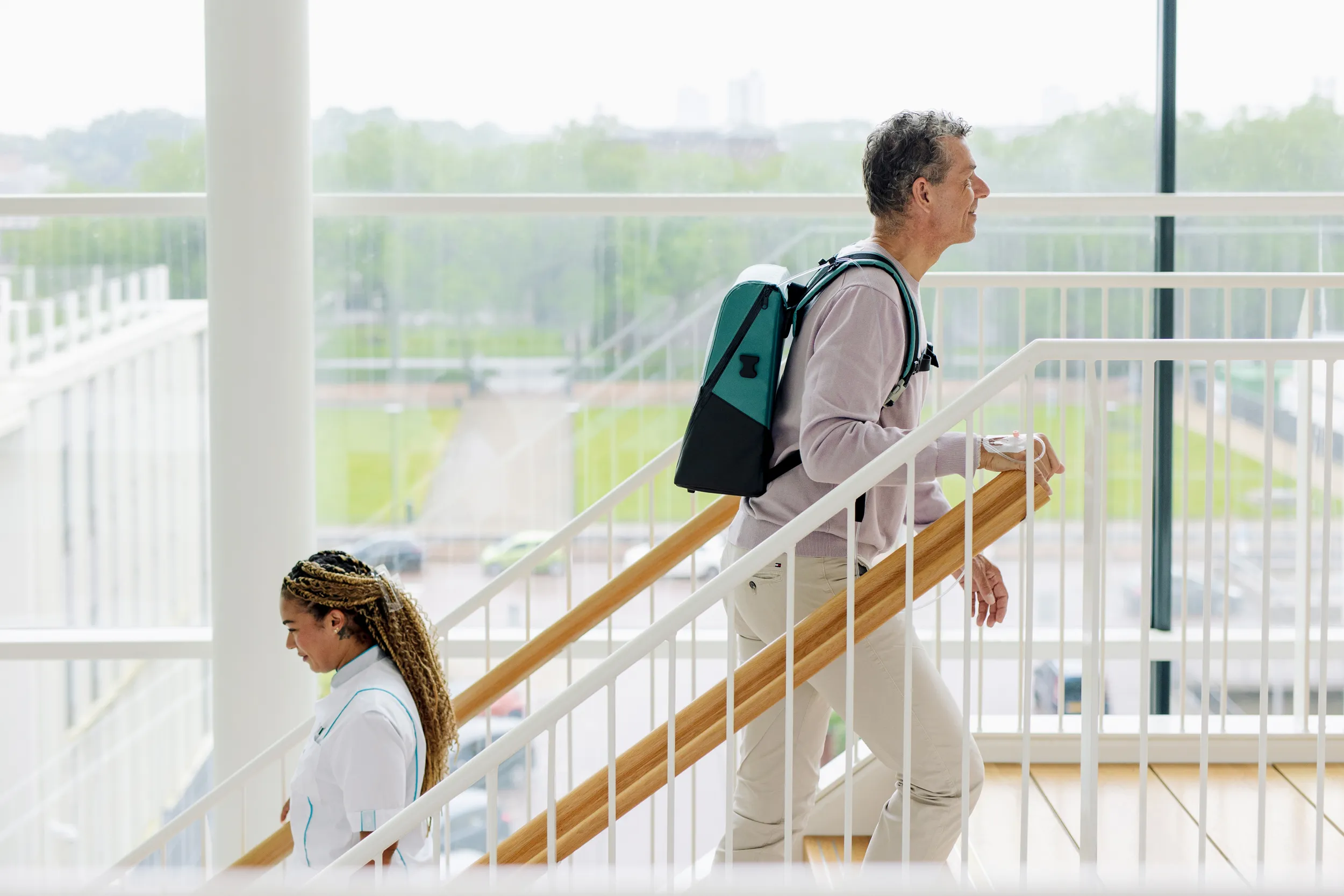 A male patient walking up the stairs while carrying the Ivy Duo+, just passing by a nurse
