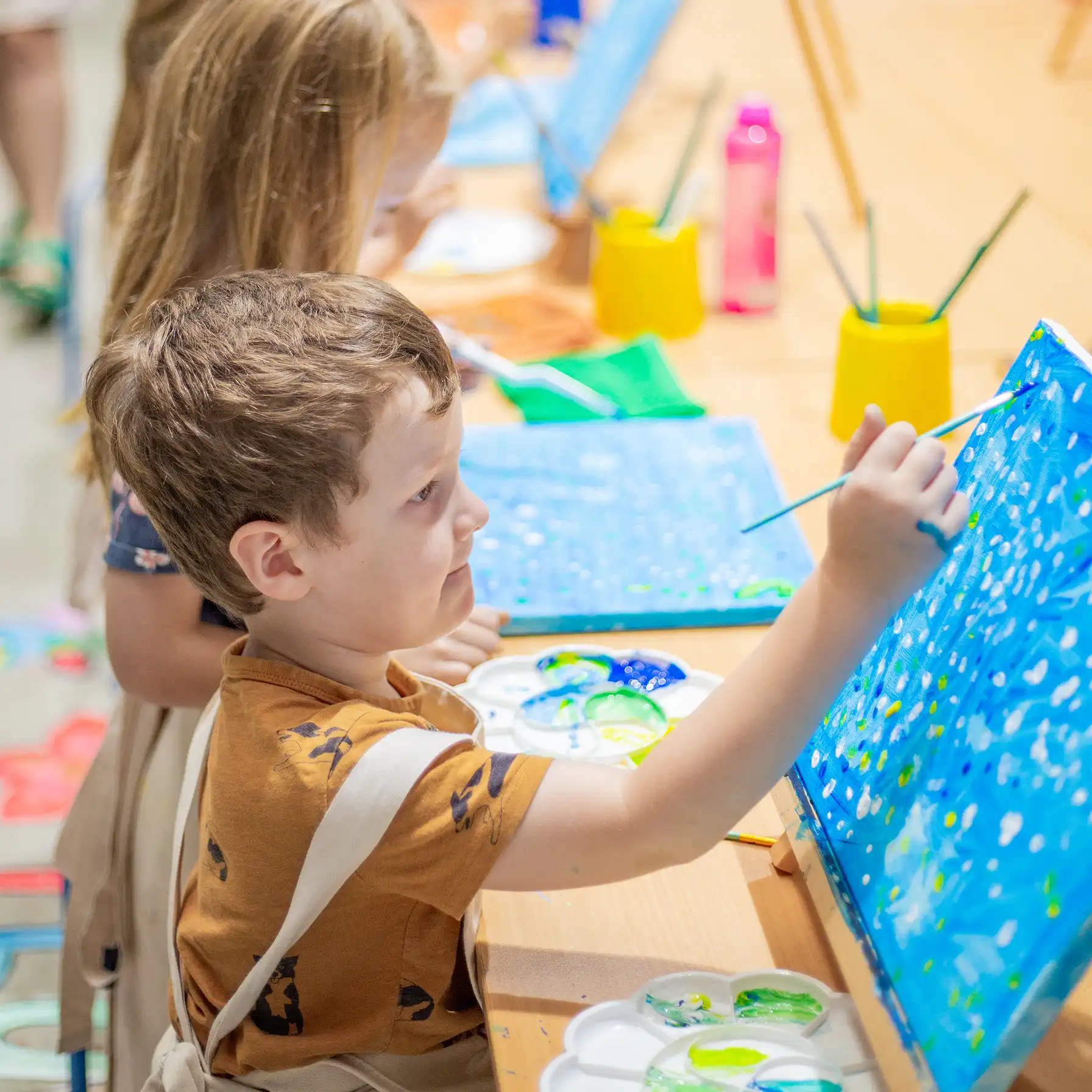 A close up of a small boy smiling and painting his canvas.