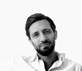 Man with dark hair and trimmed beard in a white shirt, looking casual 