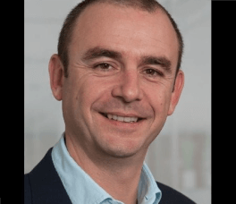 Man smiling in a light blue shirt and a black blazer 