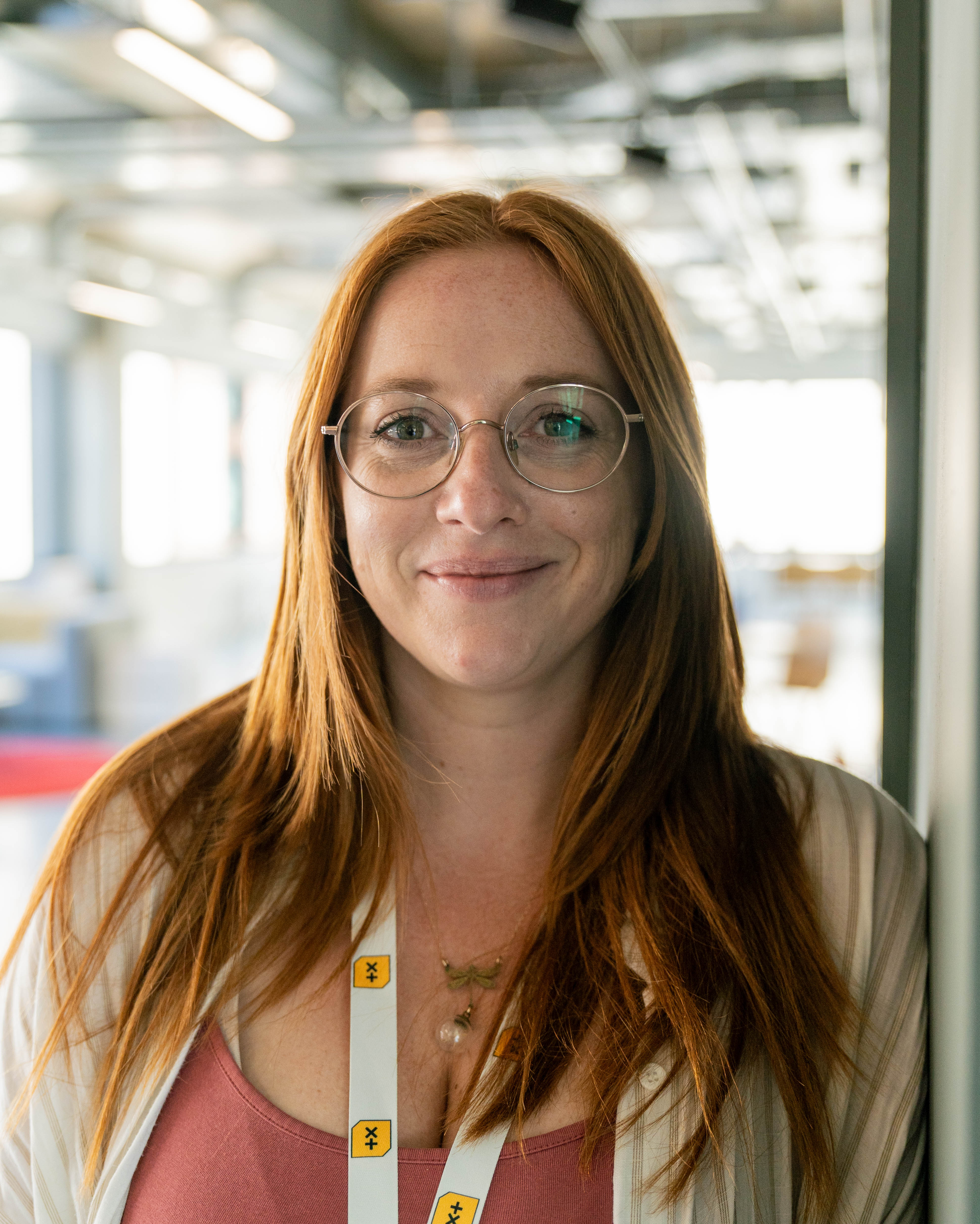 A woman smiling at the camera with glasses and ginger hair with a fringe. She is outside in front of a wall with ivy.