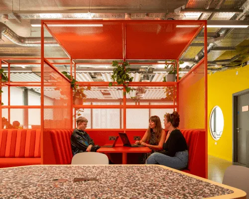 Three people working in a red booth in a coworking space at Plus X Innovation Brighton