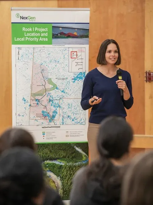 Woman holding microphone presenting Rook I Project location and priority map to seated audience.