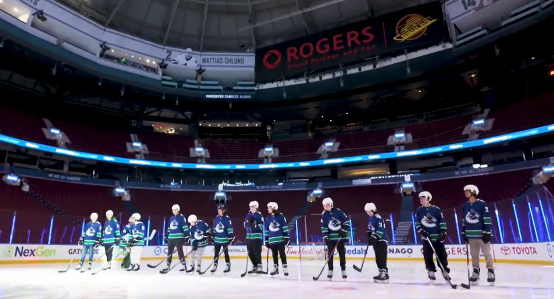 Ice hockey players in blue jerseys lined up on the rink inside a large arena.