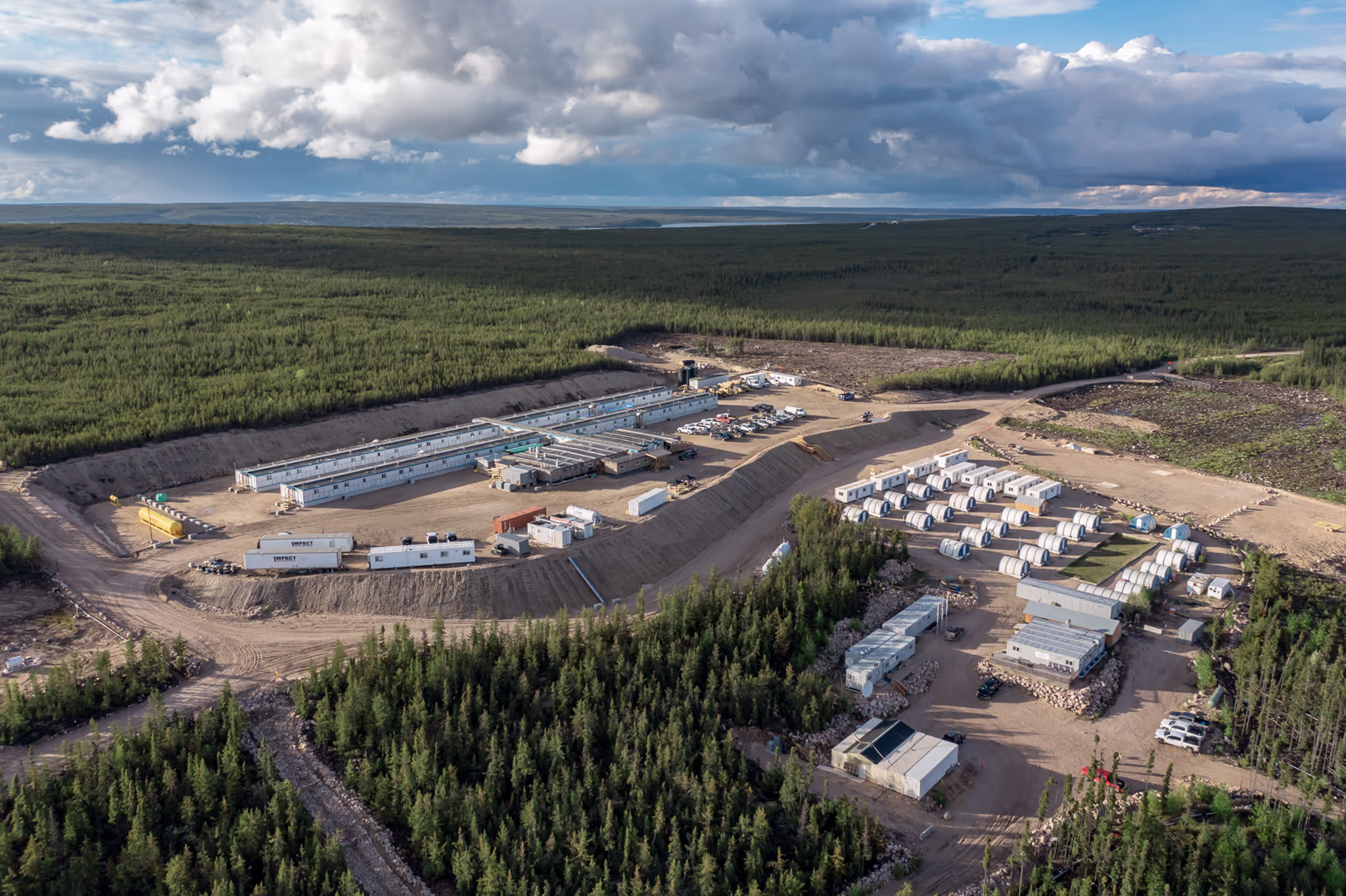 Aerial view of a remote industrial camp surrounded by forest under a cloudy sky.