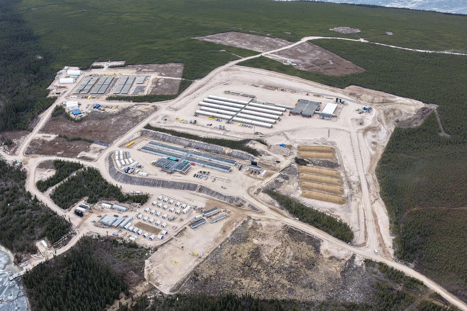 Aerial view of an industrial site with buildings, storage tanks, and dirt roads surrounded by forest.