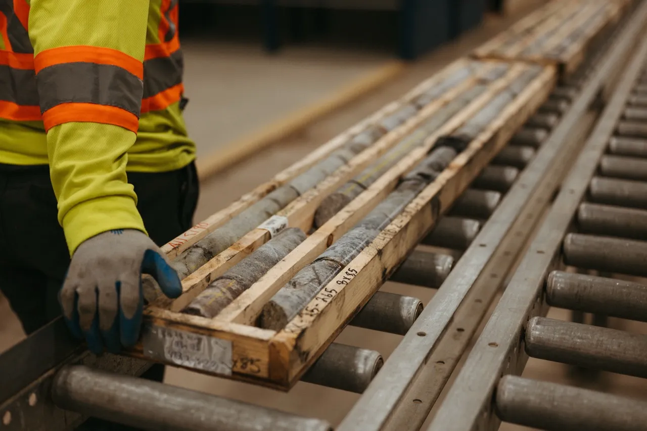 Worker in safety gear handling wooden tray with cylindrical rock core samples on rollers.