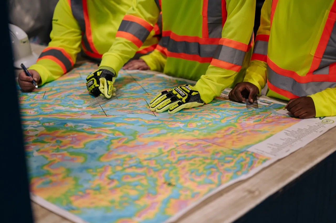 People in reflective safety gear pointing and marking a colorful topographic map on a table.