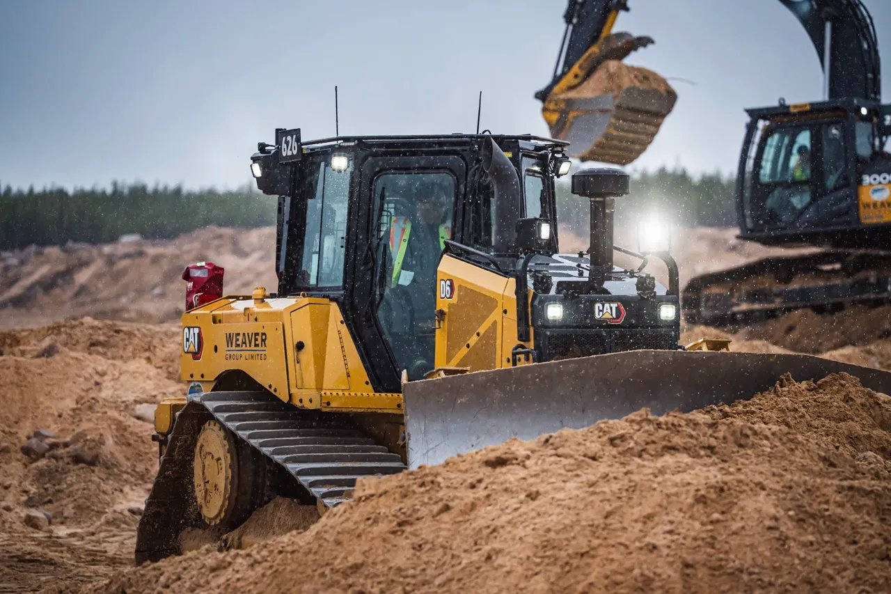 Yellow Caterpillar D6 bulldozer pushing dirt with excavator loading soil in the background.