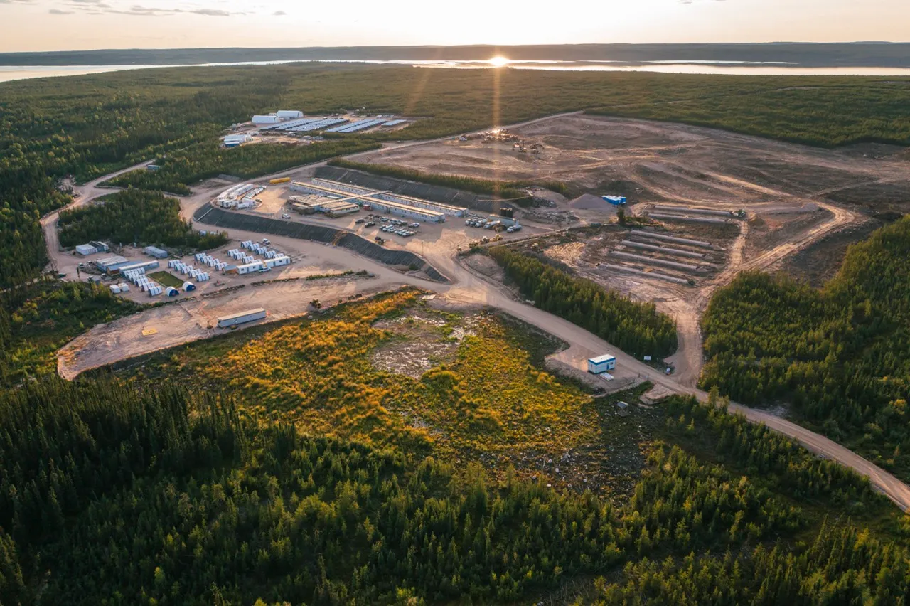 Aerial view of a construction site in a forested area at sunset with dirt roads and buildings.