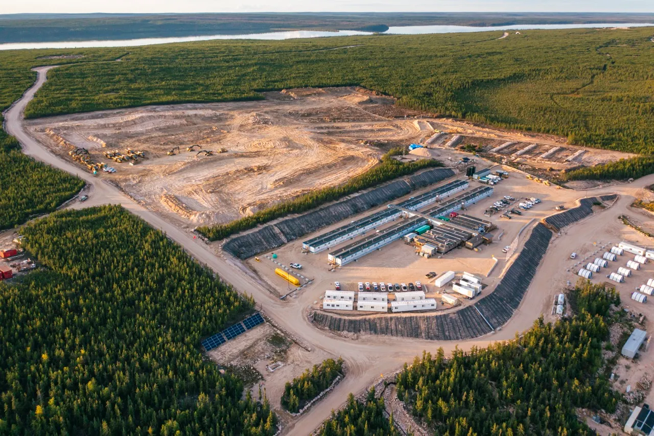 Aerial view of a large construction site surrounded by dense forest and distant water body.