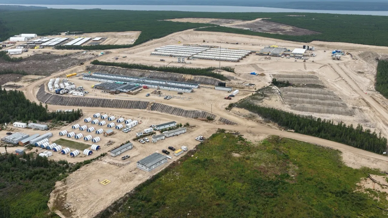 Aerial view of a large construction site with temporary buildings, cleared land, and forest surrounding it.