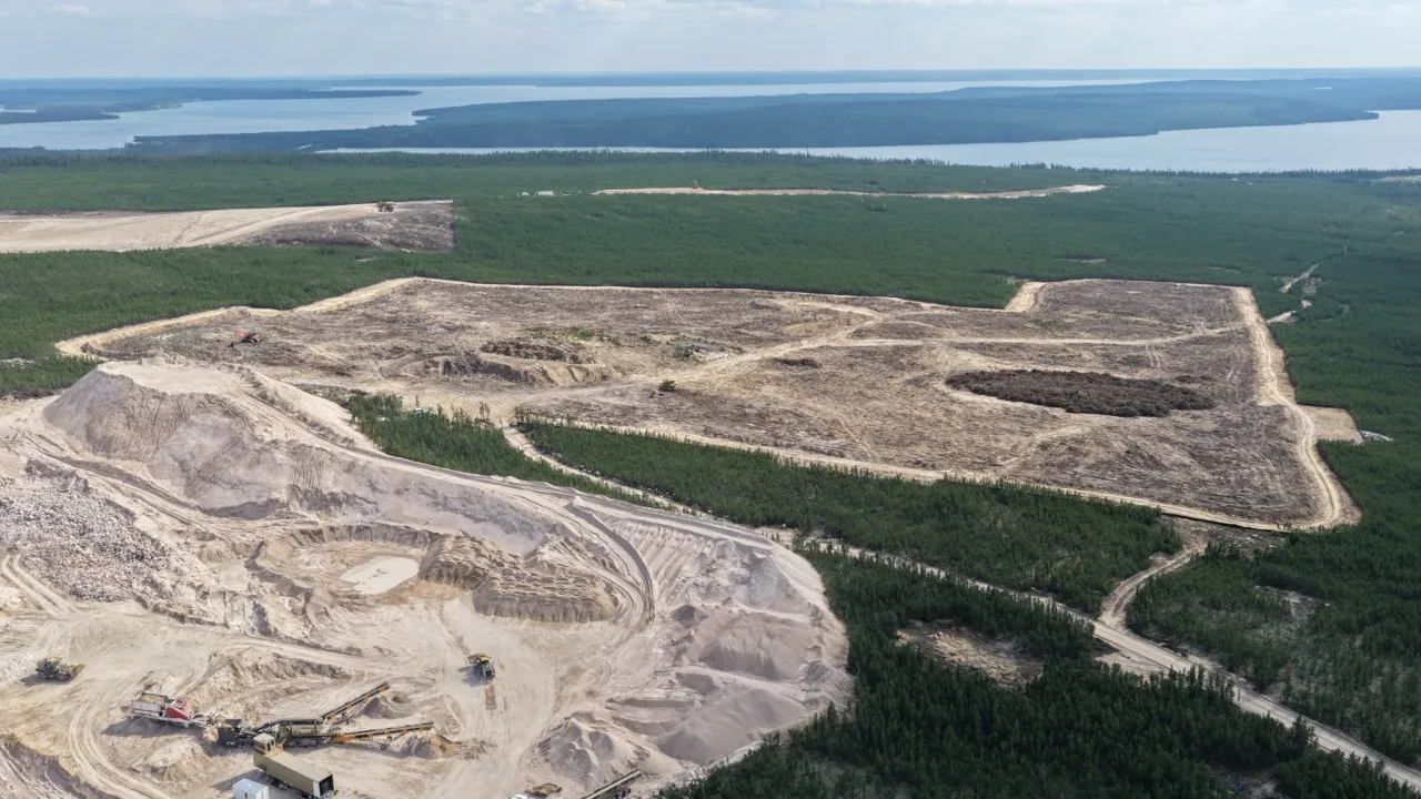 Aerial view of a large cleared mining site surrounded by dense green forest and distant water bodies.