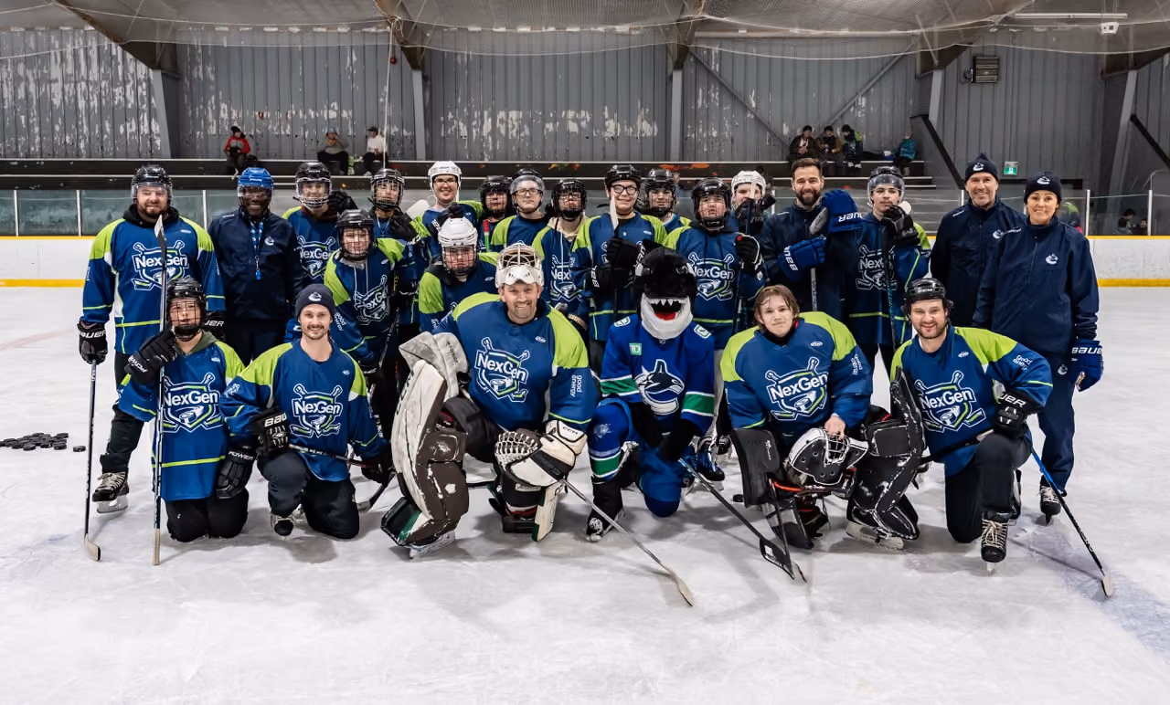 Group photo of hockey team in blue and green NexGen jerseys with mascot on ice rink.