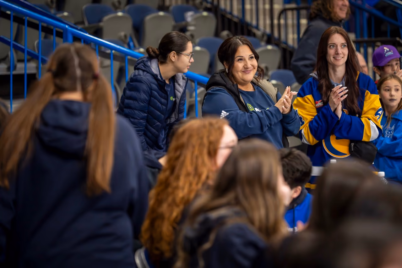 Group of people in blue and yellow clothing clapping and smiling at an indoor event with stadium seating.