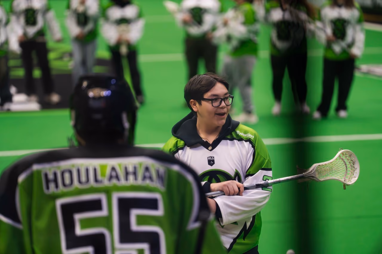 Lacrosse player in glasses holding a stick speaking to a player wearing number 55 jersey with 'HOULAHAN'.
