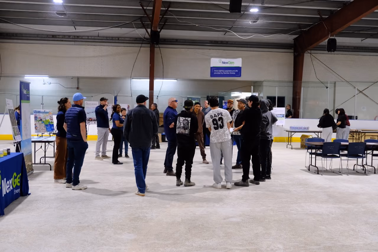 Group of people standing and talking inside an indoor ice rink with NexGen Energy displays.