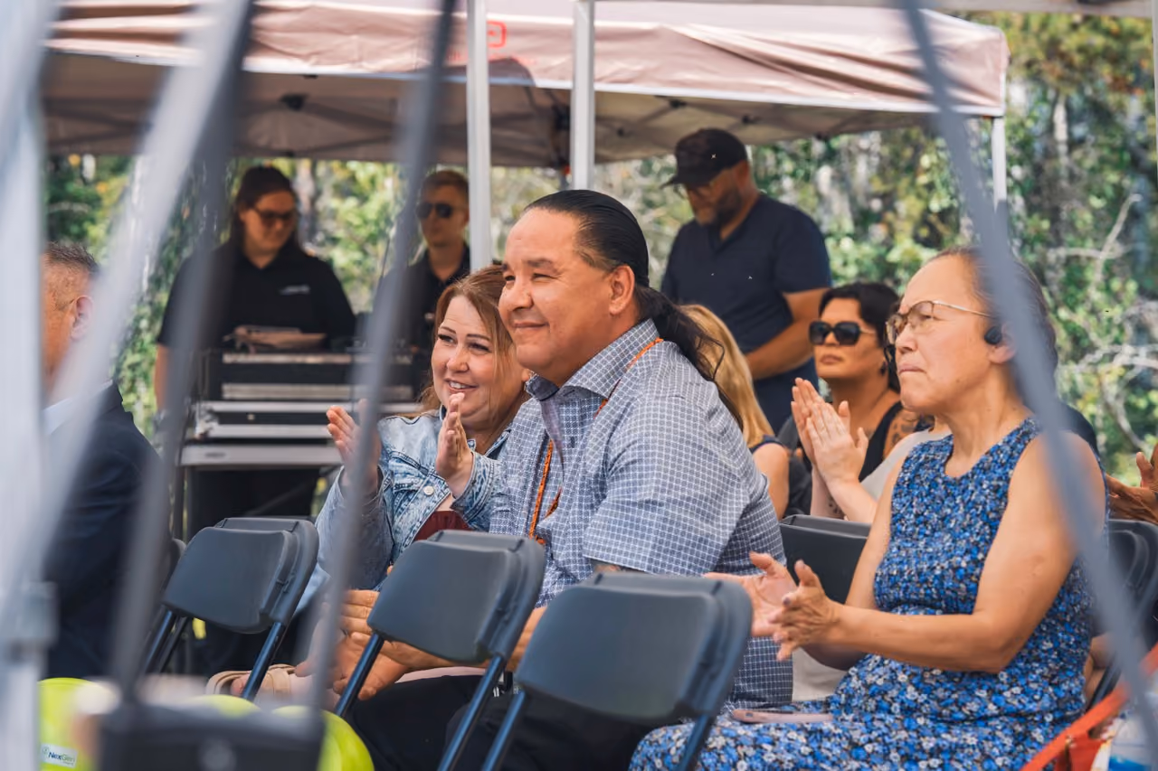 Group of people sitting and clapping outdoors under a canopy during an event.
