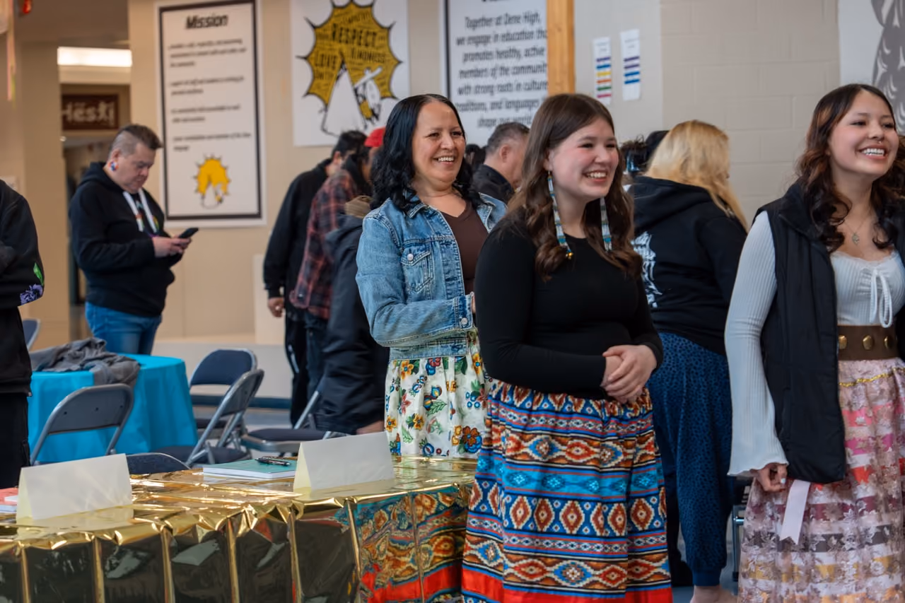 Smiling young women and a woman gather indoors near tables with gold covers at a community event.