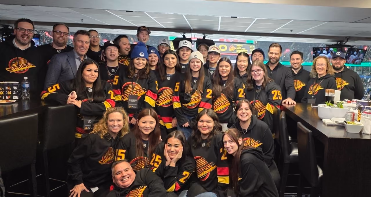 Large group of people in black Vancouver Canucks jerseys posing indoors at sports event.