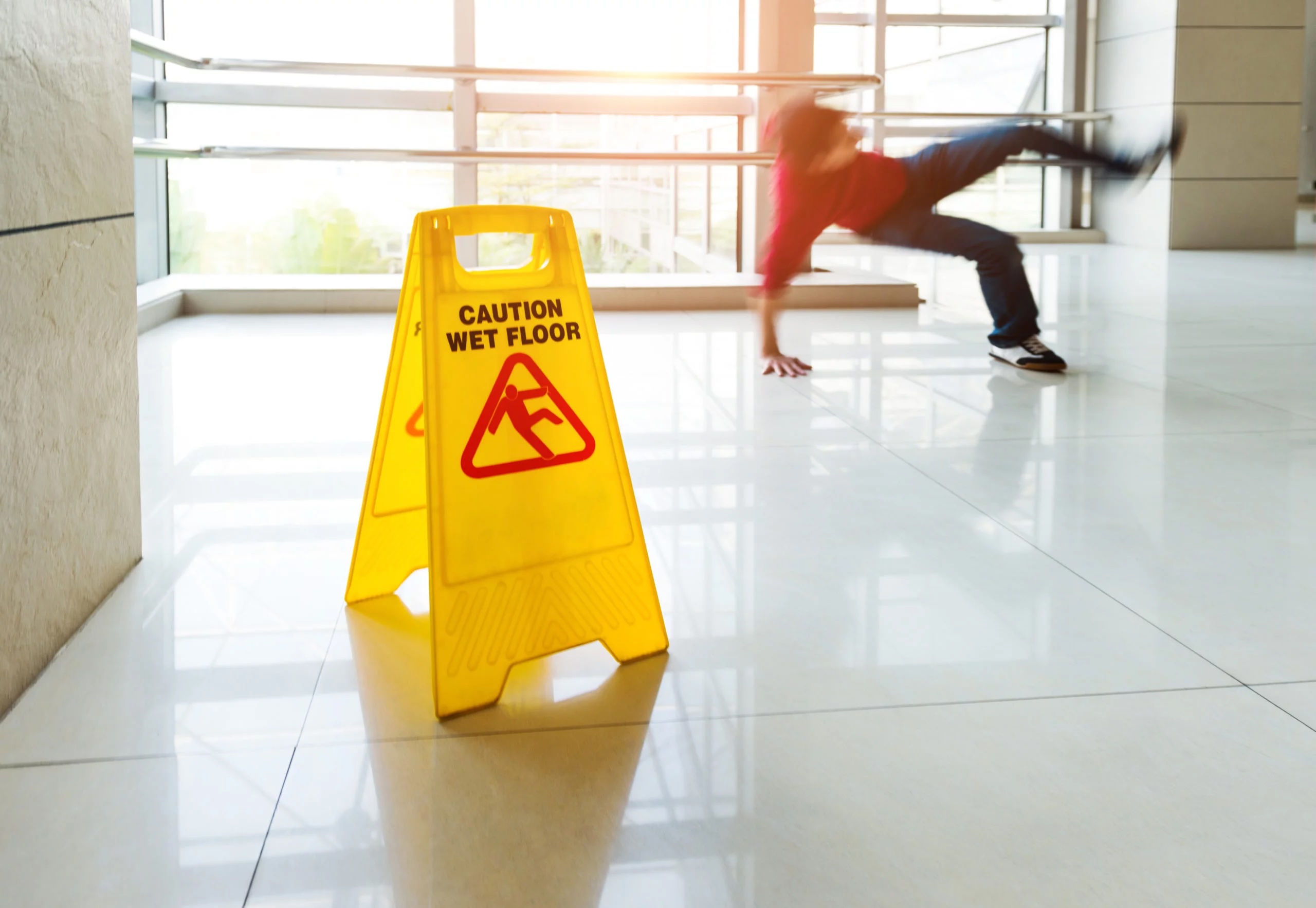 Caution wet floor sign with a person slipping and falling behind it, representing premises liability and personal injury verdicts in San Diego