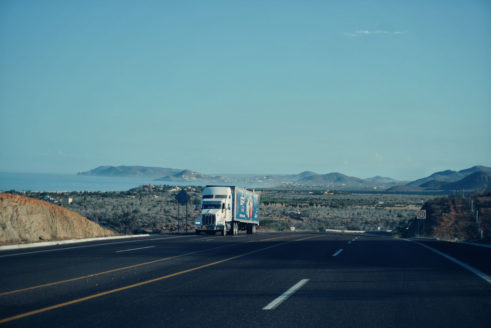 Semi truck driving on a coastal California highway with hills and ocean in the background
