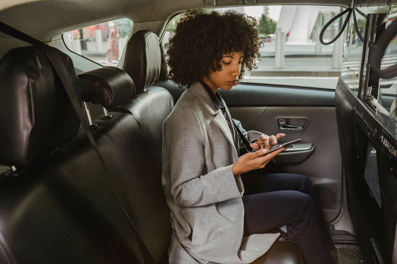 Passenger checking a rideshare app on her phone in the back seat of a car