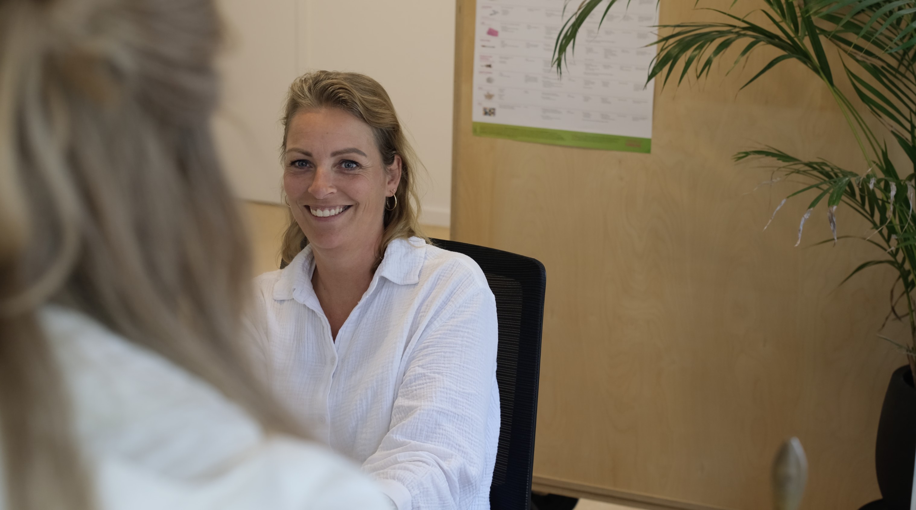 Doktersassistent in gesprek aan de balie van een huisartsenpraktijk