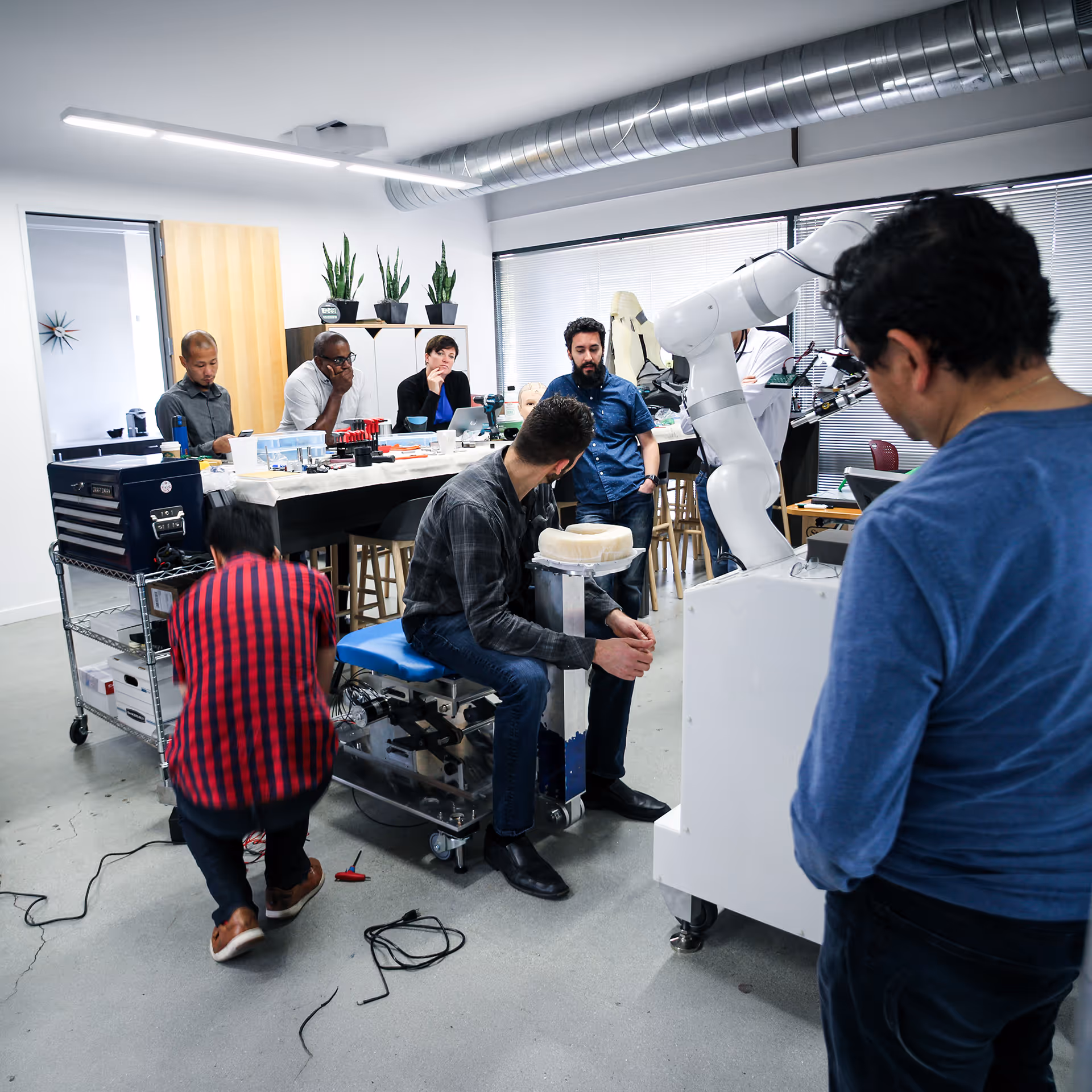 Group of people in a modern lab working around a robotic arm and technical equipment on tables and benches.