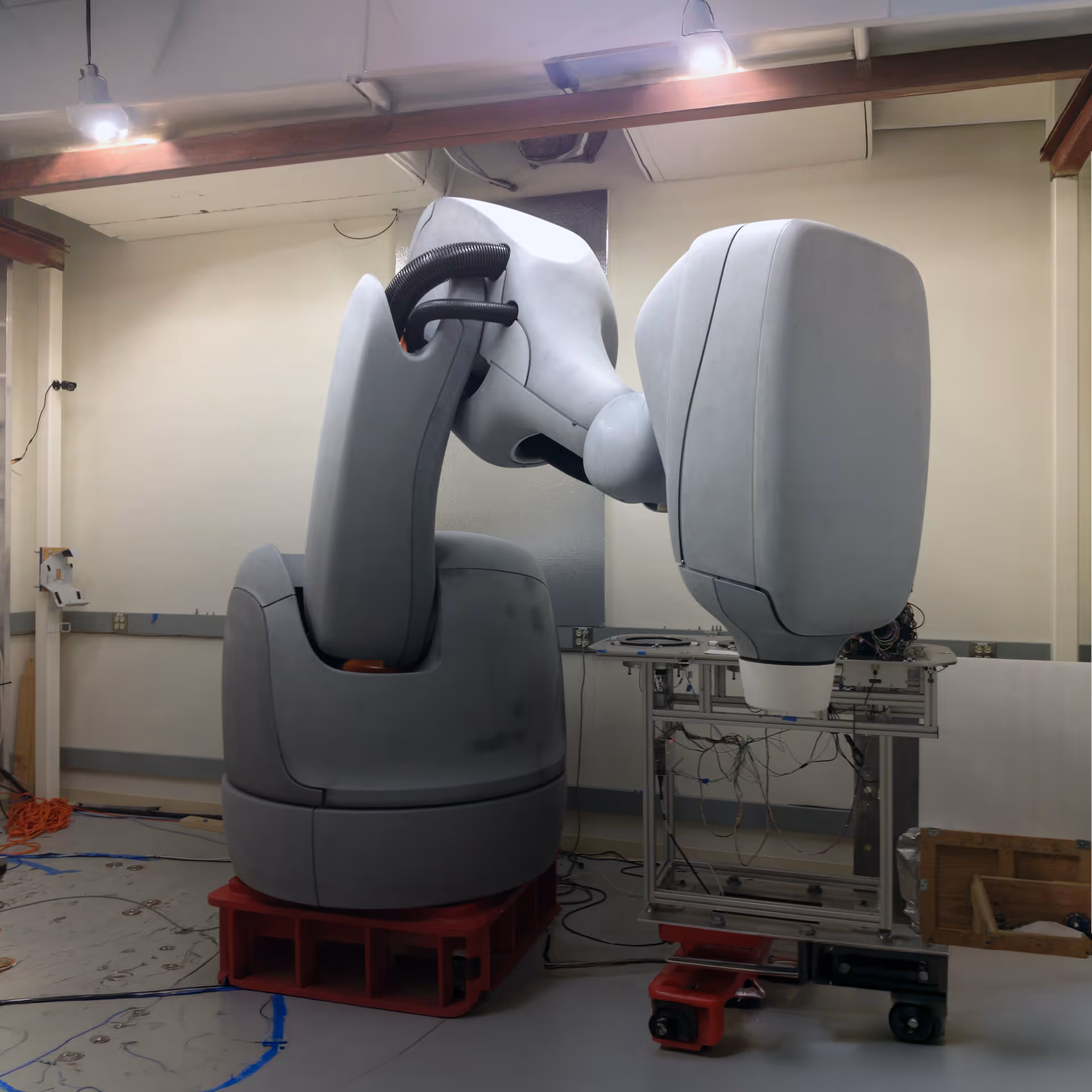 Large gray industrial robot arm indoors with wiring and equipment in background.