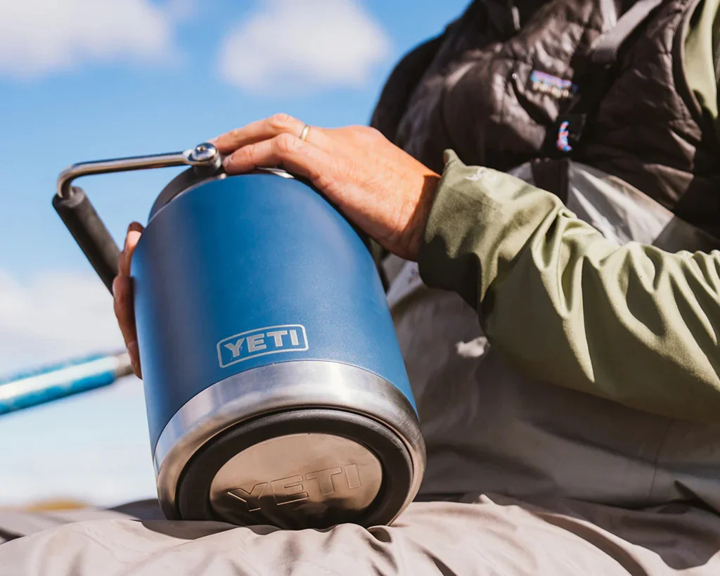 Person holding blue YETI Rambler Jug showcasing ergonomic industrial design and outdoor durability