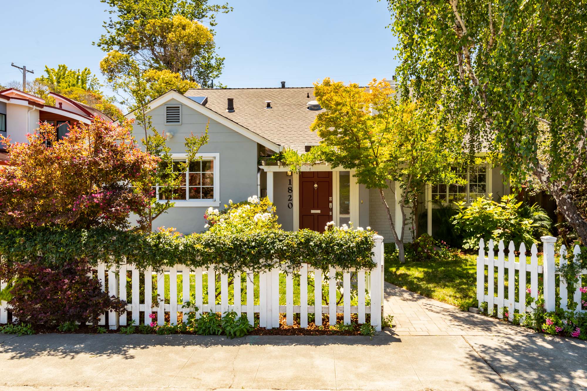 A charming house surrounded by a white picket fence and a lush green tree in the yard.