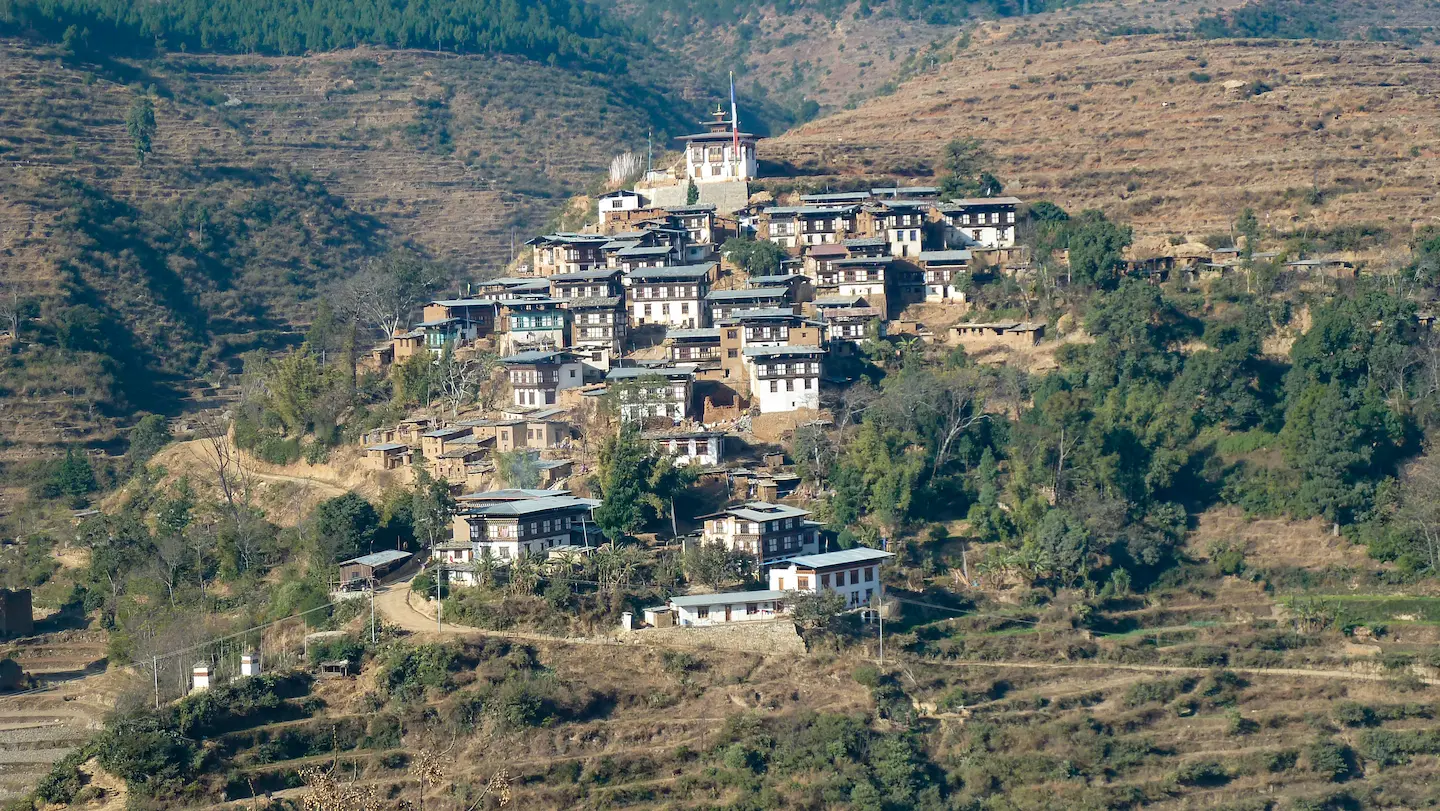 Ein malerisches Dorf, eingebettet in die Hügel mit traditionellen Gebäuden, umgeben von terrassierten Landschaften und üppigem Grün.